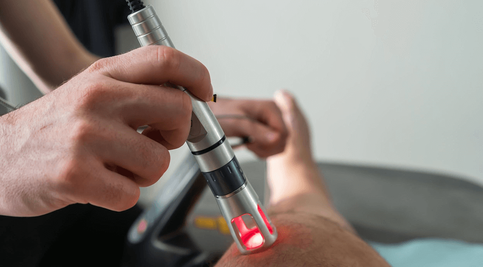 A specialist using an applicator with a red laser on a patient’s leg