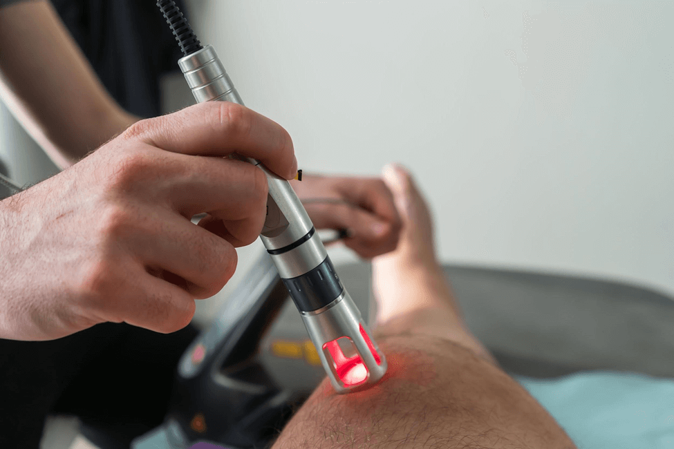 A specialist using an applicator with a red laser on a patient’s leg