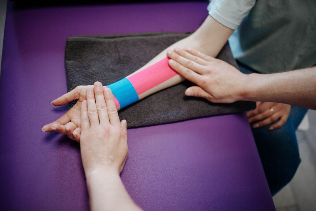 A physiotherapist placing blue and pink Kinesio tapes on a person’s arm.