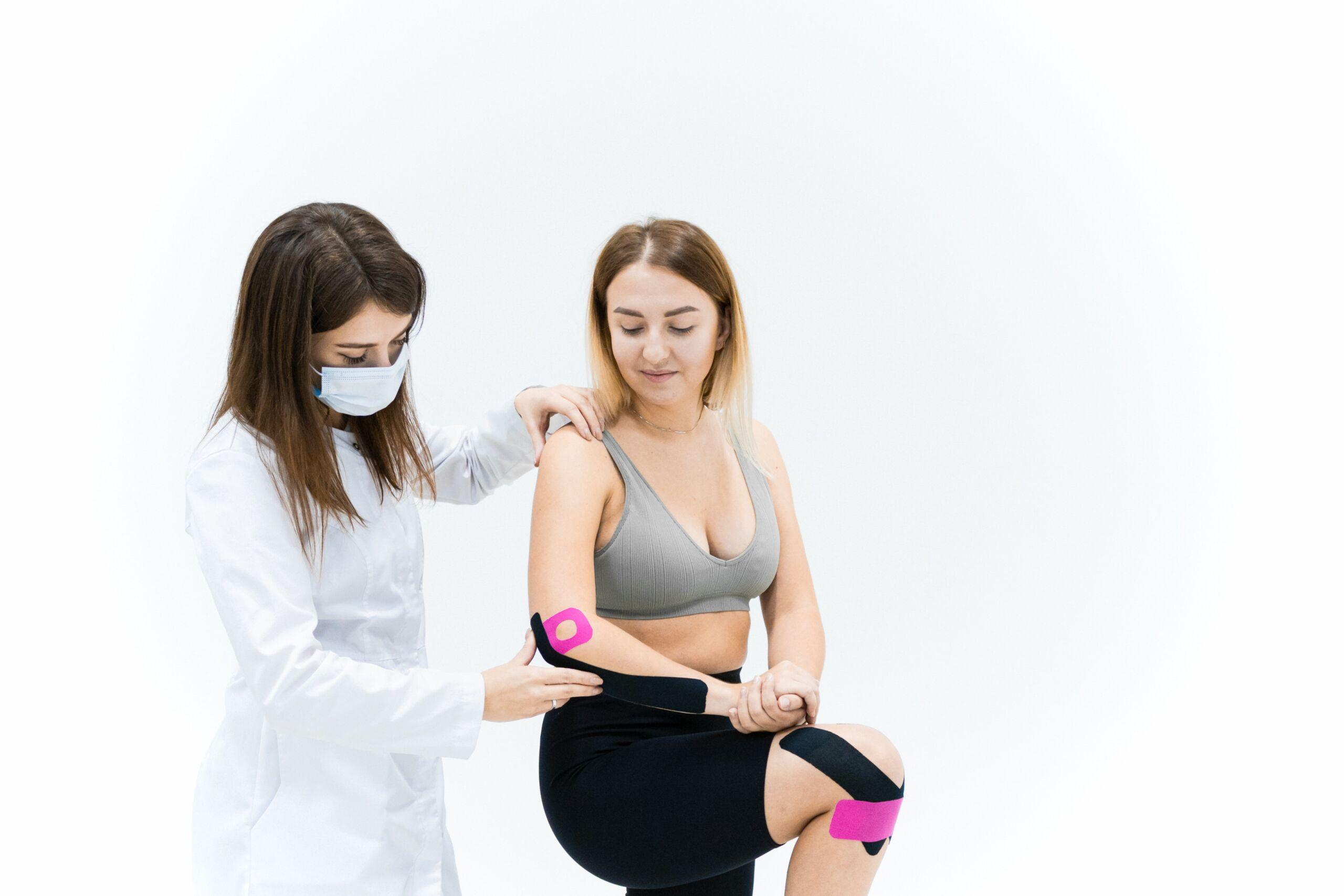 A doctor helping a patient standing with Kinesio tape on their elbow and knee. 